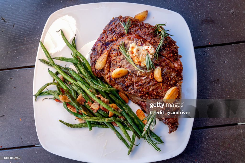 Charcoal Grilled Ribeye Steak Medium Rare Plated With A Side Of Sauteed Green Beans With Bacon And Garlic