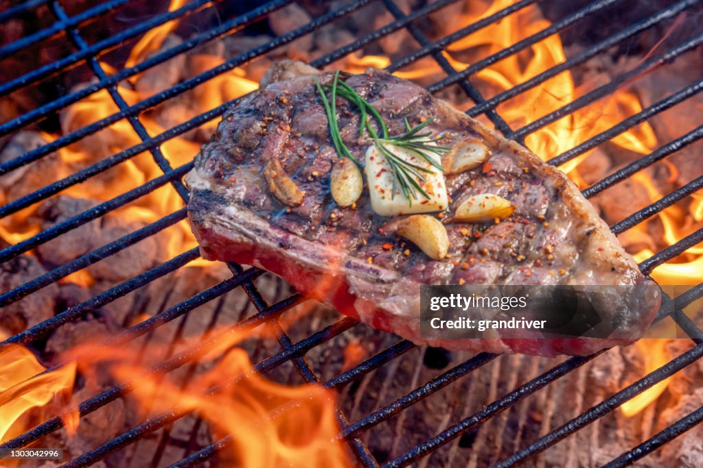 Gegrilltes Ribeye Steak auf einem heißen Kohlegrill mit Flammen gekrönt mit sauteed Knoblauchzehen ein Pat Butter und Rosmarin