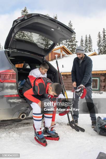 a father helps two brothers put on their ice-hockey equipment - hockey car stock-fotos und bilder