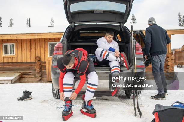 brothers in hockey equipment pull their ice skates on - outdoor ice hockey stock pictures, royalty-free photos & images