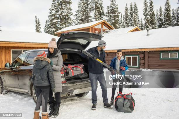 family unloads hockey from trunk at winter vacation cabin - hockey car stock-fotos und bilder