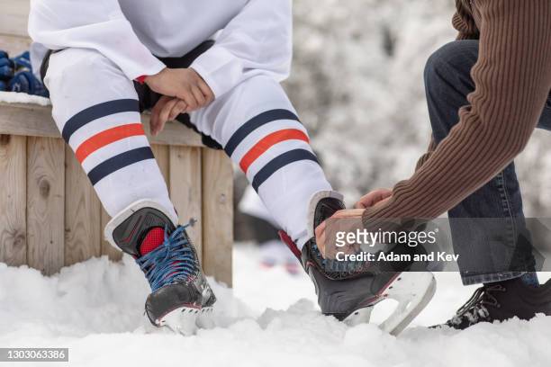 adult hands tying laces of adolescent's ice-skates at outdoor rink - hockey skating stock pictures, royalty-free photos & images