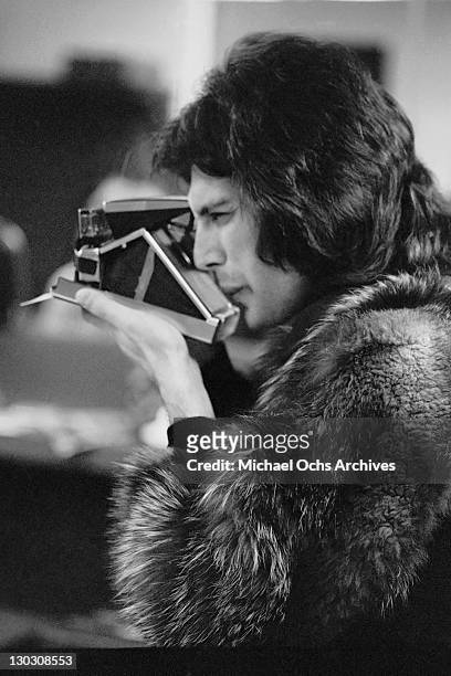 Singer Freddie Mercury of British rock band Queen takes a Polaroid, Los Angeles, US, circa 1977.