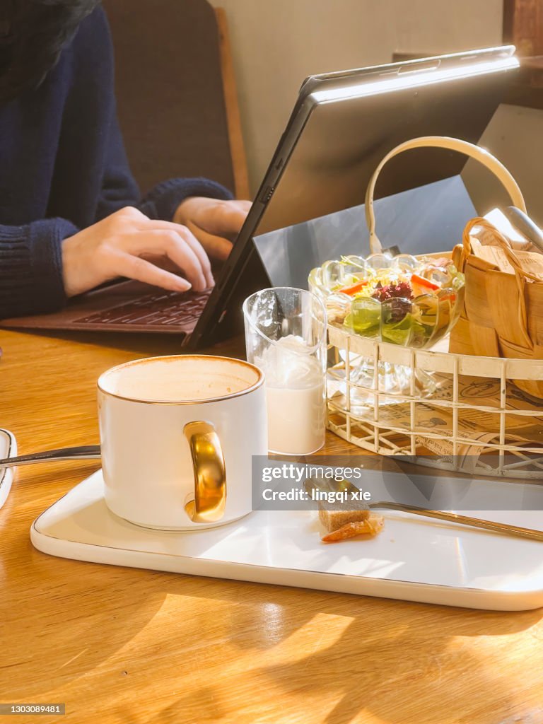 A girl is using a laptop for office, coffee and bread are on the table