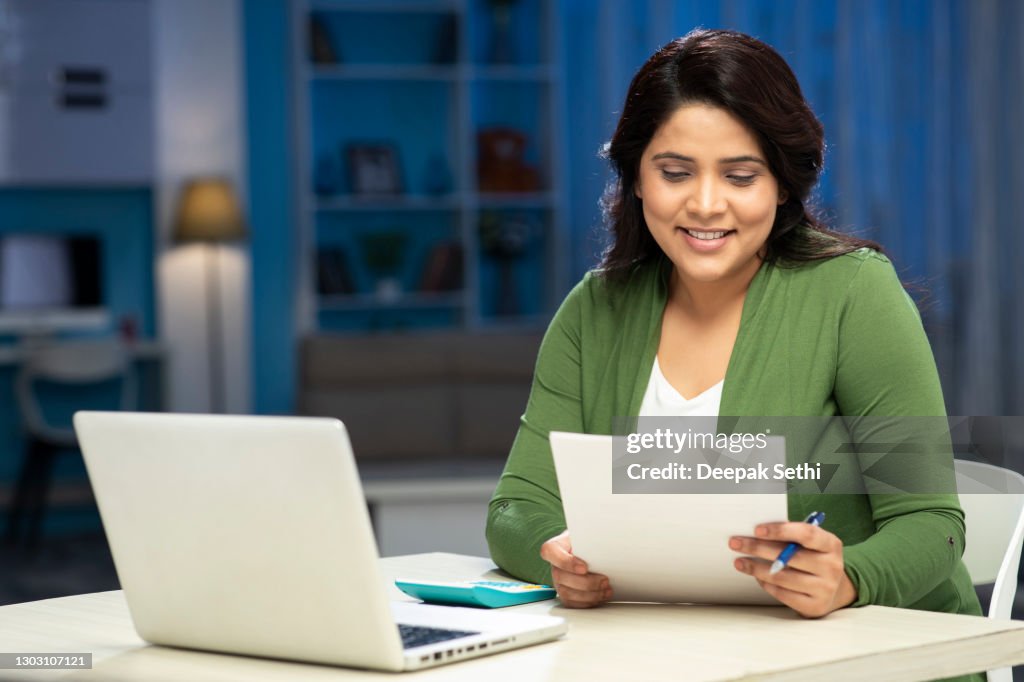 Mid adult women examine document and calculating expenses using laptop at home, stock photo