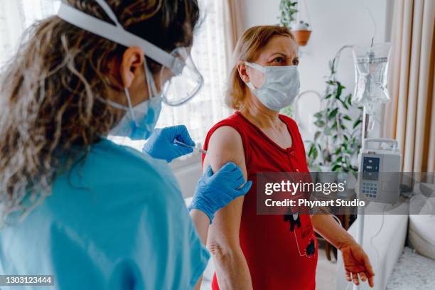 vrouw die een vaccin van haar arts in haar huis krijgt tijdens een huisbezoek tijdens de covid-19-pandemie. - infuus stockfoto's en -beelden