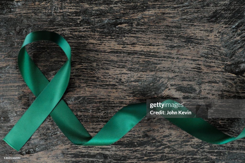 Top view of emerald green ribbon on dark wood background. Liver cancer awareness concept.