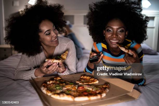 vriendinnen die op bed liggen en pizza eten - african family watching tv stockfoto's en -beelden