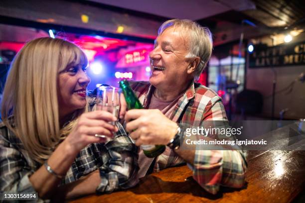 senior-paar sitzt an der bartheke und hat spaß date nacht in nachtclub - boomer couple out on town stock-fotos und bilder