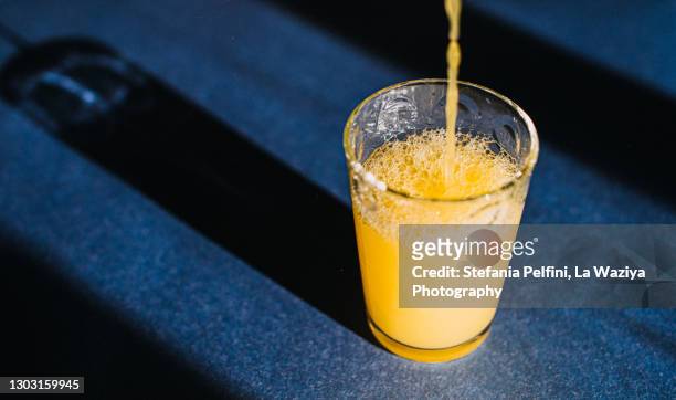 orange juice being poured in a glass that casts a beautiful shadow on a blue surface. - orange juice stock pictures, royalty-free photos & images