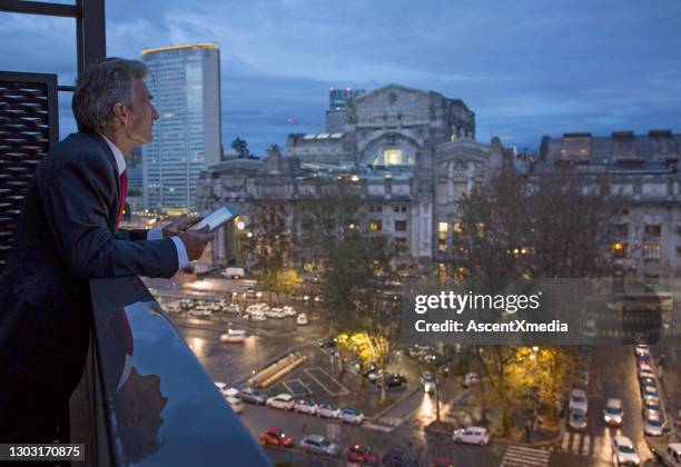 businessman checks digital tablet on balcony above city, night - milan skyline stock pictures, royalty-free photos & images