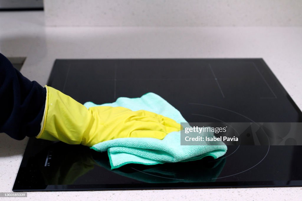 Close-up of hand with rubber glove cleaning induction stove with rag