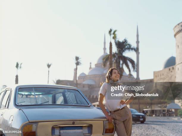 vrouw in hoofddoek die zich dichtbij de uitstekende auto op de achtergrond van moskee van muhammad ali bevindt - caïro stockfoto's en -beelden