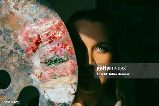 an artist with a palette on her face looks into the camera. - schilder kunstenaar stockfoto's en -beelden