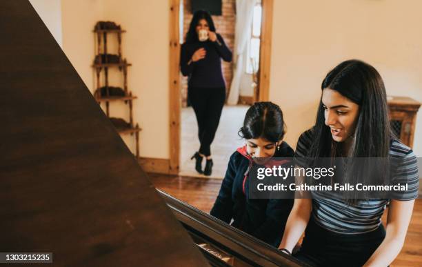 two sisters play the piano together while mum watches - arabic keyboard fotografías e imágenes de stock