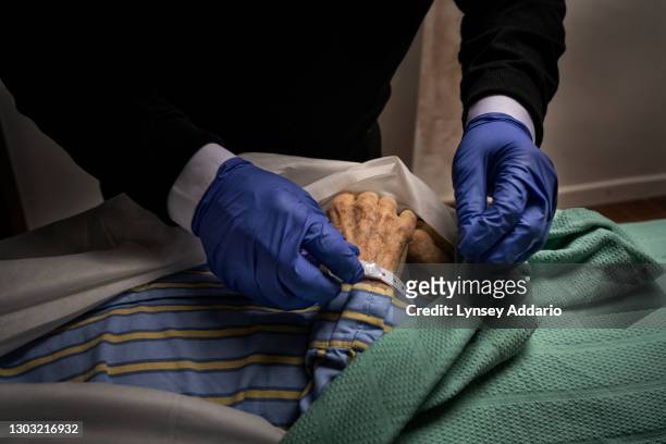 An employee of Taunton Funeral Services attaches a name tag to the wrist of a patient who died that morning of suspected COVID-19 in a nursing home...