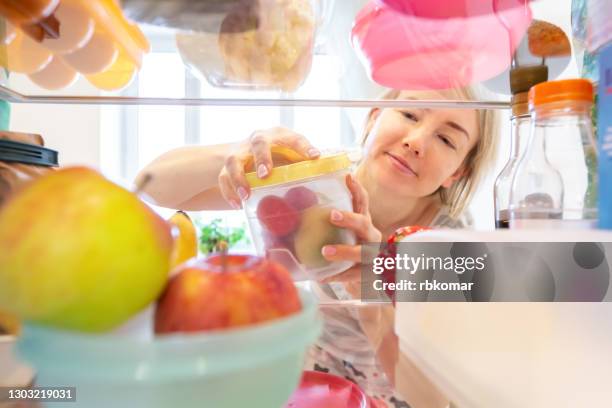 young contented woman opens a plastic box of vegetables with radishes, inside view from a full refrigerator with food - lagerhaltung stock-fotos und bilder
