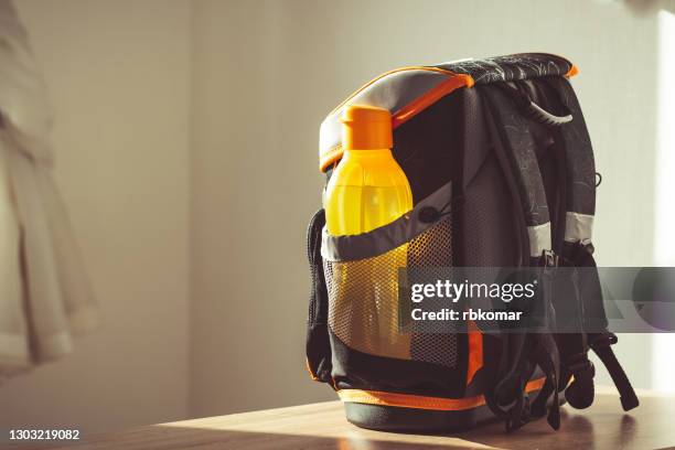 a ready-made kids' black and orange elementary school backpack with a reusable water bottle on the table in the classroom. back to school, new school year, start of learning - リュックサック ストックフォトと画像