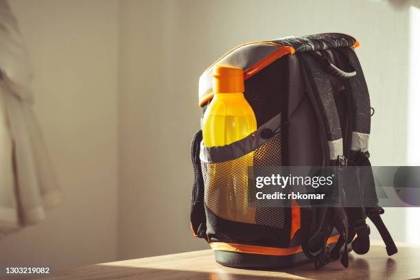 a ready-made kids' black and orange elementary school backpack with a reusable water bottle on the table in the classroom. back to school, new school year, start of learning - satchel stock pictures, royalty-free photos & images