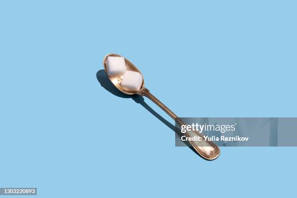 sugar cubes in a spoon on the blue background - sugar spoon stock pictures, royalty-free photos & images