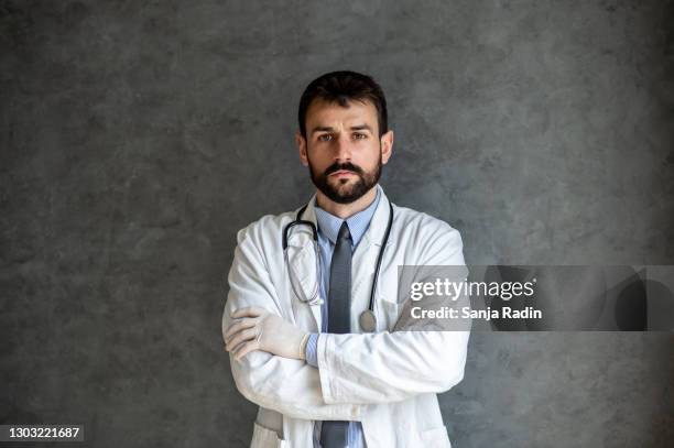 doctor with arms crossed is standing. gray background. - doctor coat stock pictures, royalty-free photos & images