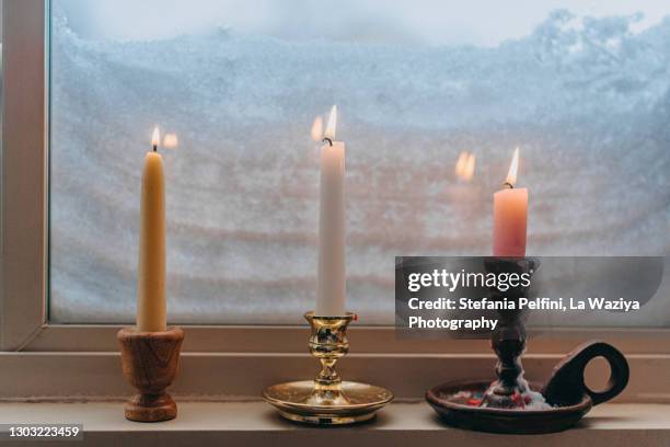 three lit candles on a window sill completely covered with snow - candle light foto e immagini stock