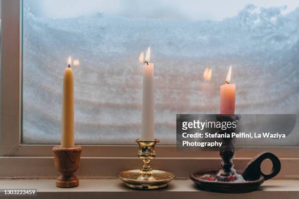 three lit candles on a window sill completely covered with snow - candle light stock pictures, royalty-free photos & images