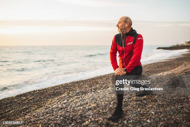 senior adult male runner stretching legs and warming up outdoors before running training - runner warming up stock pictures, royalty-free photos & images