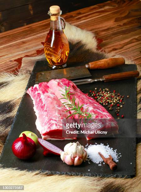 detail raw wild boar meat on a black plate with garlic, rosemary, onion salt, pepper and olive oil. - wildbret stock-fotos und bilder