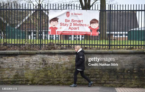 Lady walks past social distancing signage displayed onto a school gate at St Saviour's Academy Primary School on February 21, 2021 in Talke, United...