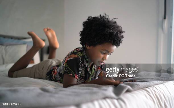 jongen die in bed ligt dat spelende spelen op digitale tablet thuis - children on a tablet stockfoto's en -beelden