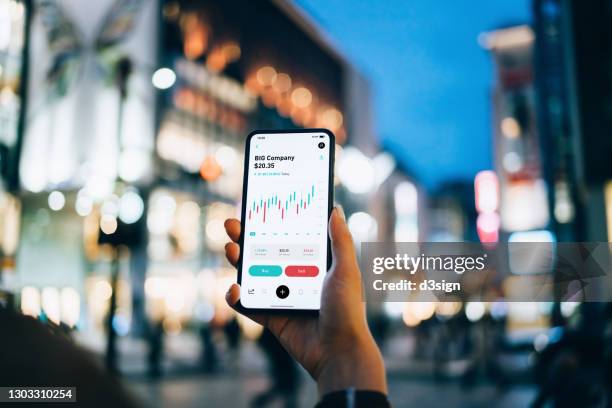 close up of businesswoman reading financial stock market analysis on smartphone on the go, in downtown city street against illuminated urban skyscrapers in the evening. business on the go - bitcoin trading stock pictures, royalty-free photos & images