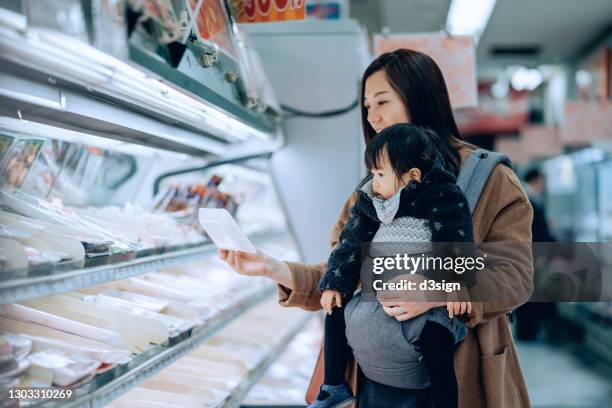 young asian mother doing grocery shopping with adorable little daughter. she is choosing for fresh poultry along the refrigerated aisle in a supermarket - fish love imagens e fotografias de stock