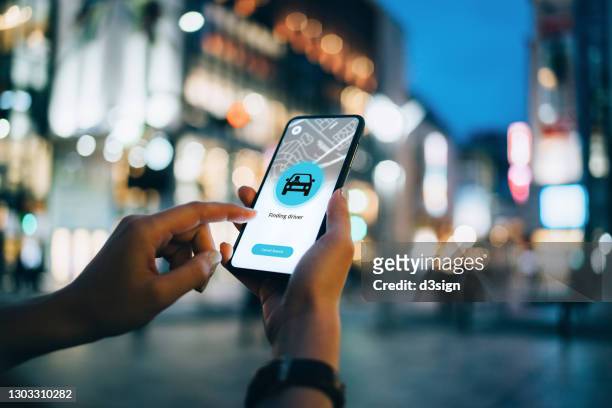 close up of young woman using mobile app device on smartphone to arrange a taxi ride in downtown city street, with illuminated city traffic scene as background - apps fotografías e imágenes de stock