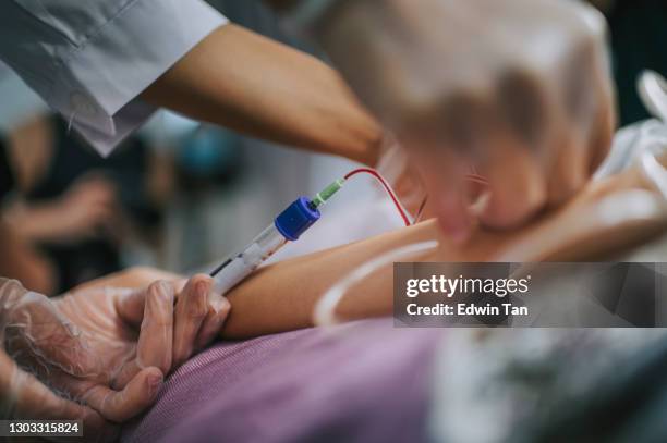 close up asian chinese nurse drawing blood from female chinese patient arm's vein in the clinic - blood bank stock pictures, royalty-free photos & images