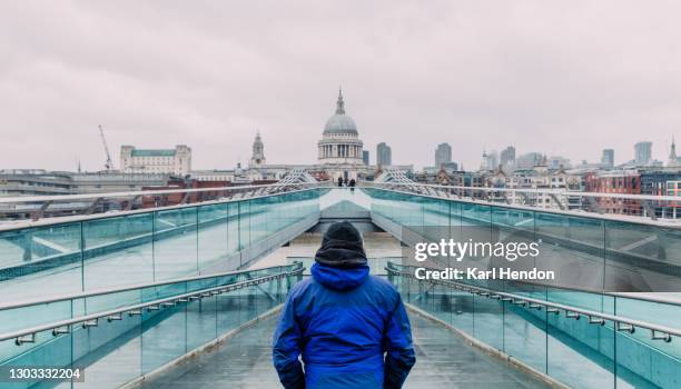 a man stands looking at saint paul's cathedral in london on a snowy day - stock photo - millennium bridge stockfoto's en -beelden