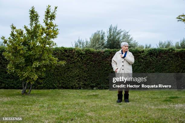 caucasian senior woman with arm sling walking in the garden - agony in the garden stockfoto's en -beelden