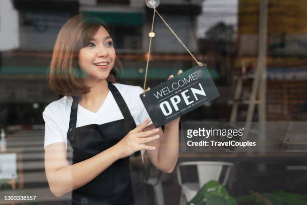 asian woman waitress holding open sign in cafe bar flipping hanging on door window. small business owner and startup with cafe shop. installing open and close label concept - open sign on door stock-fotos und bilder