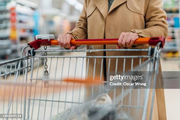 cropped shot of young woman with shopping cart in supermarket - shopping cart groceries stockfoto's en -beelden