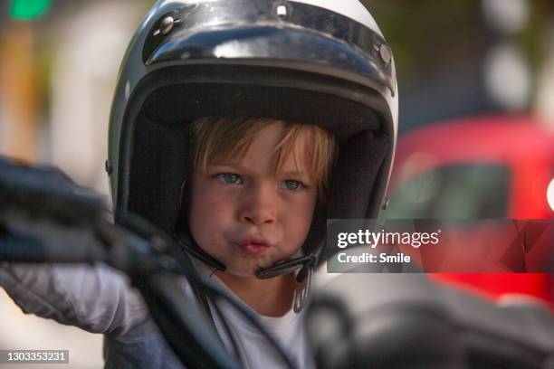 handsome young boy pretending to ride motorcycle - crash helmet stock-fotos und bilder