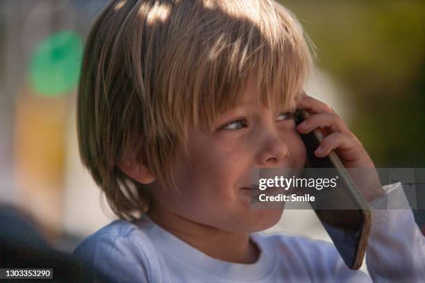 cute happy blond boy holding a cell phone to his ear listening to whatever's said - child listening differential focus stock pictures, royalty-free photos & images