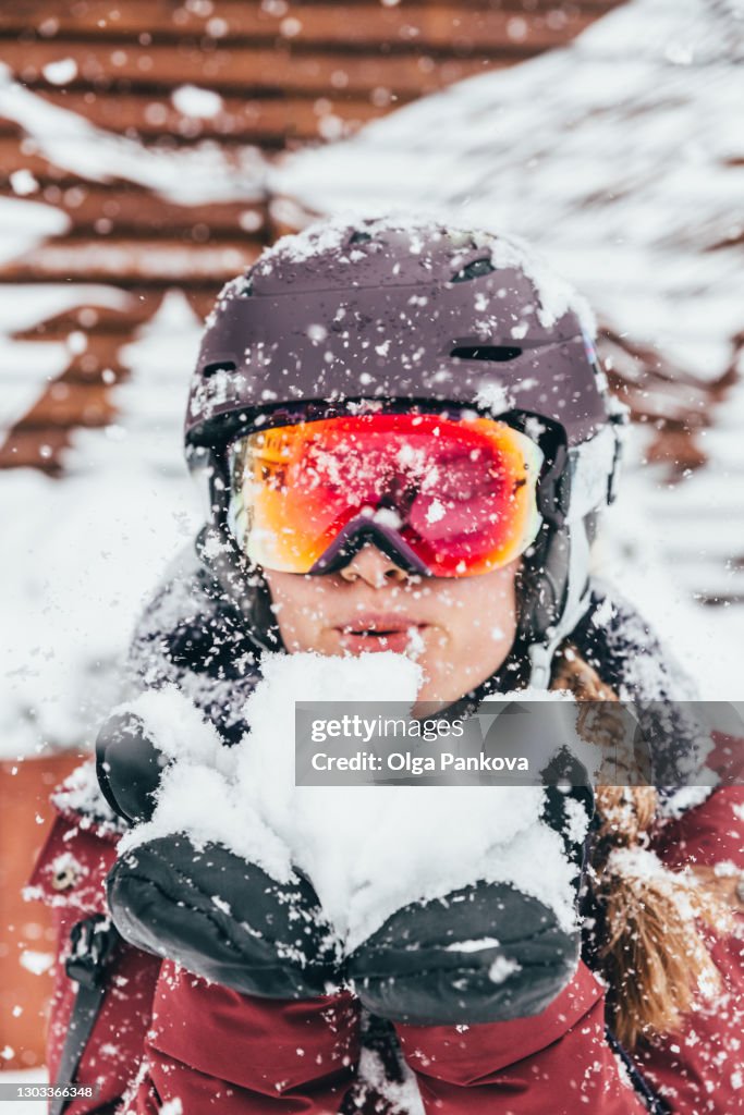 Young woman dressed in snowboard jacket, helmet and ski goggles has fun on snowy day.