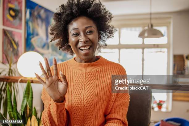 ritratto di sorridente giovane afroamericana al chiuso che parla con la telecamera, videochiachiarica, registra vlog - sventolare la mano foto e immagini stock