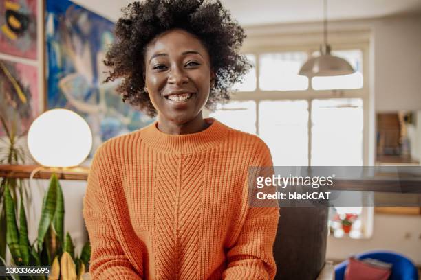 portrait of smiling african american young woman indoors talking to camera, video calling, recording vlog - eastern european woman stock pictures, royalty-free photos & images
