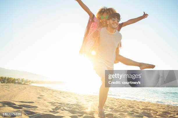 paar dat piggyback op het strand bij zonsondergang of zonsopgang speelt. - malaga walking stockfoto's en -beelden