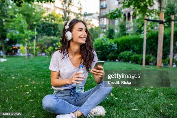 jonge vrouwenzitting op het gras in park en het ontspannen - woman smartphone nature stockfoto's en -beelden