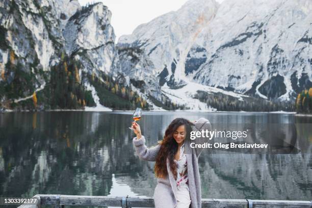 happy woman enjoying with glass of wine on background of lago di braies lake in winter - mountains alcohol snow bildbanksfoton och bilder