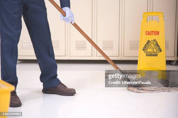 senior adult janitor mops floor in office building.  he wears a protective face mask. - serviços de limpeza imagens e fotografias de stock