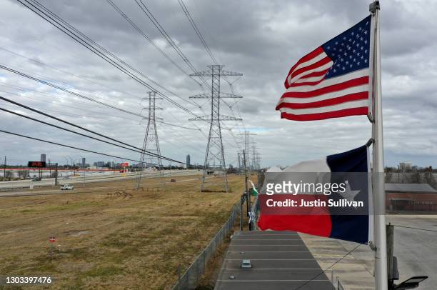 The U.S. And Texas flags fly in front of high voltage transmission towers on February 21, 2021 in Houston, Texas. Millions of Texans lost power when...