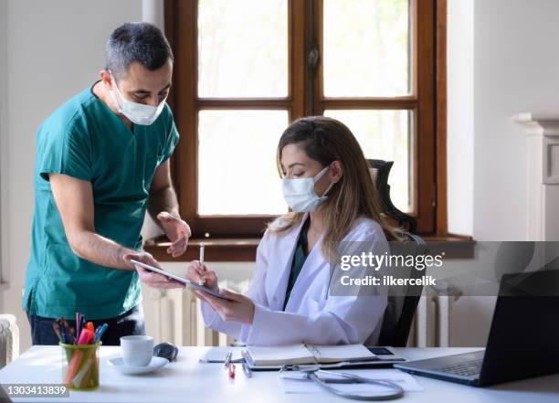 portrait of female and male doctors discussing with positive emotions in clinic using digital tablet and stylus - covid dating stock pictures, royalty-free photos & images